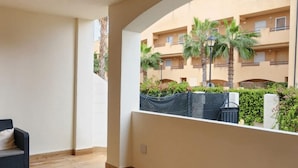 A spacious balcony with a view of a building and palm trees. There are several black wicker chairs and a small table. - Sea View - Ground Floor - Pool - Beachaccess (Vera)