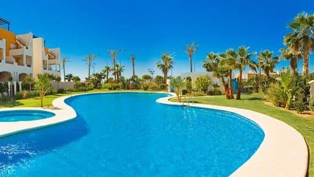 A swimming pool with a curved design, surrounded by a well-maintained lawn and palm trees. - Sea View - Ground Floor - Pool - Beachaccess (Vera)