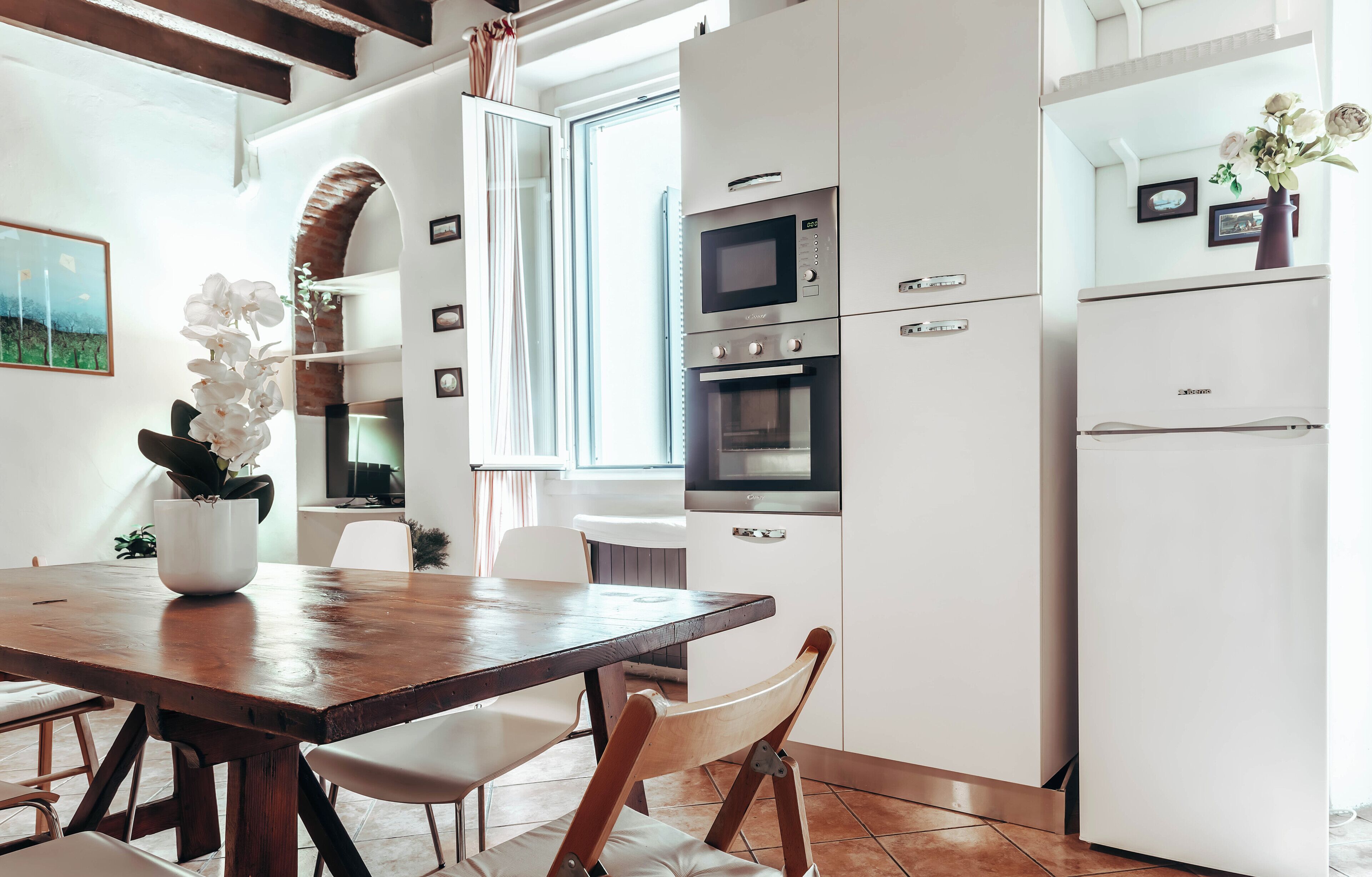 Une cuisine moderne avec des meubles blancs, une table à manger en bois et un réfrigérateur blanc.