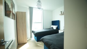 A modern bedroom with two beds, a wooden wardrobe, a radiator, and a window with curtains.