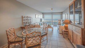 A spacious living area with a glass dining table, wicker chairs, a sofa, and a view of the sea. - Apartment in Knokke-heist With Sea Views (Knokke-Heist)