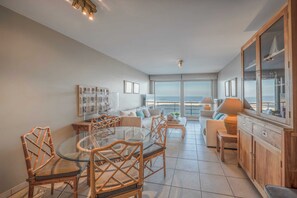 A spacious living area with a glass dining table, wicker chairs, a sofa, and a view of the sea.