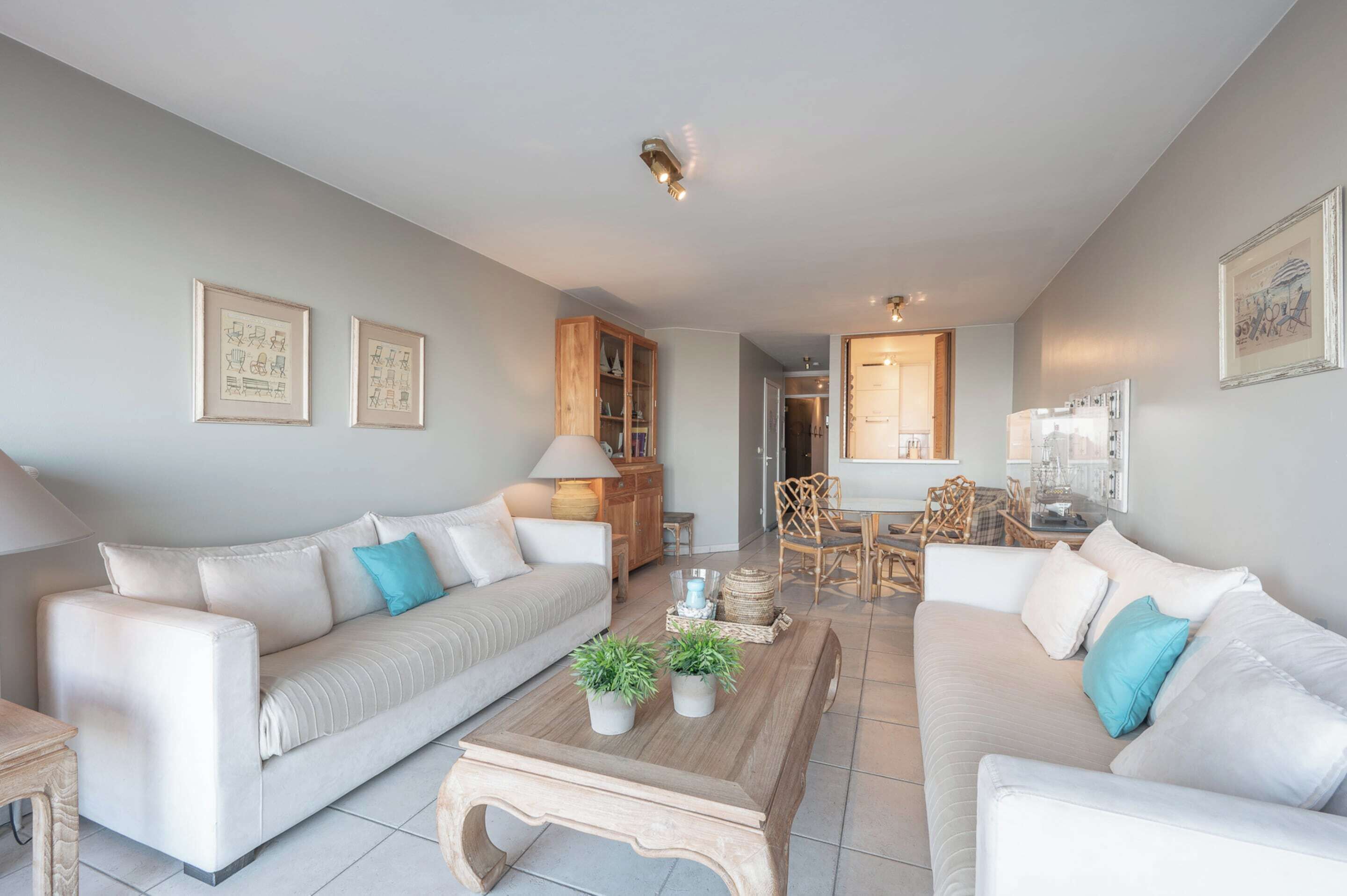 A modern living room with two sofas, a coffee table with plants, a wooden cabinet, and a dining area with chairs.
