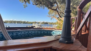 A wooden deck with a pool, a lamp post, and a view of the water and dock area. - Pellicanus House. Waterfront Paradise+Pool+Hot Tub+ Kayaks Adventure! (Palm Bay)