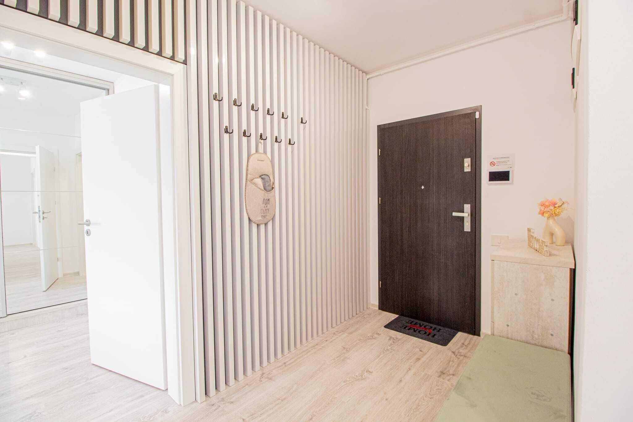 Een hotelentree met een witte muur, een donkerhouten deur en een schoenenrek met verschillende schoenparen.