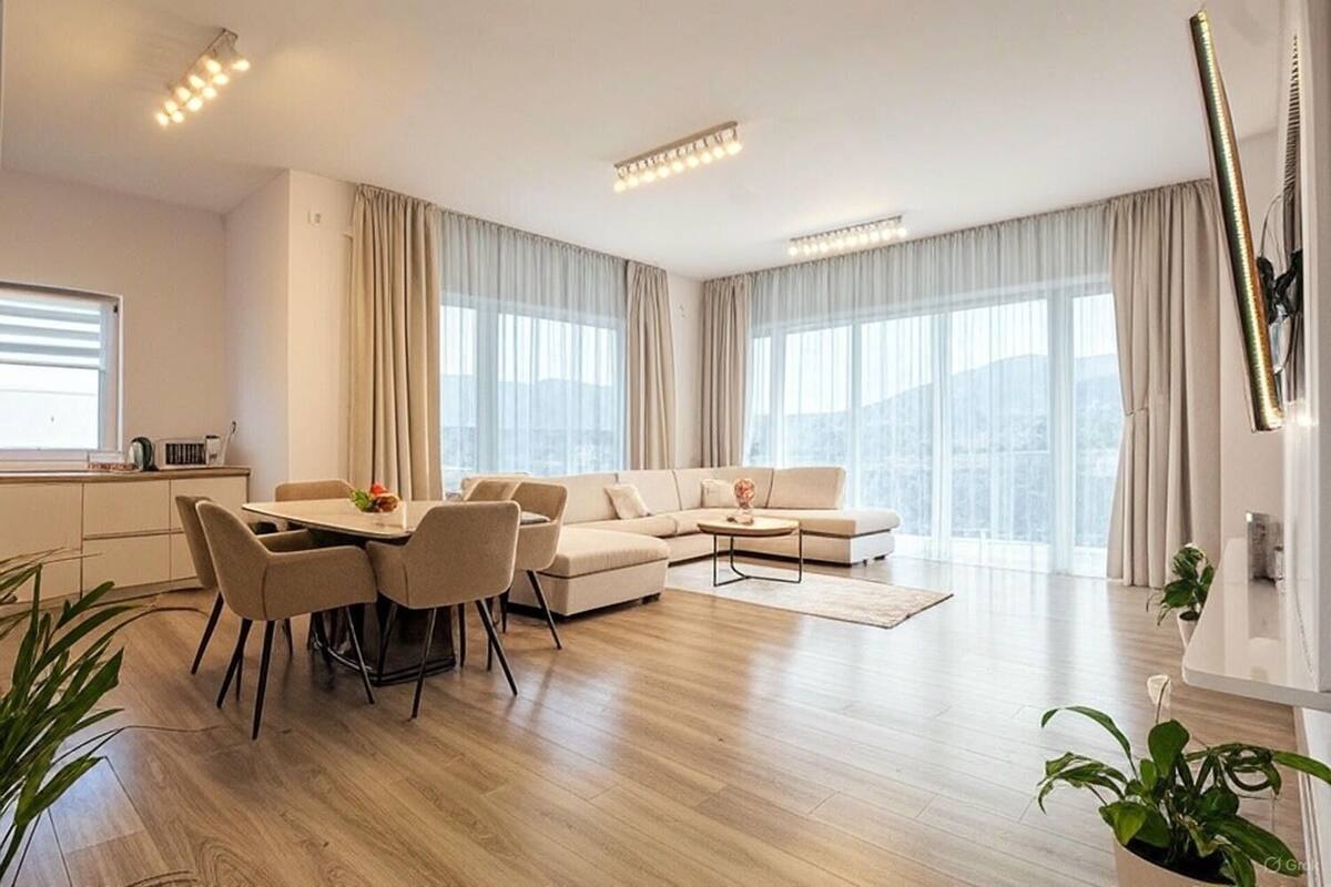 A modern living room with a dining area, large windows, and a view of the city.