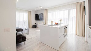 Een moderne keuken met een centraal eiland, een zithoek met een bank en een groot raam met gordijnen.