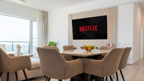 Een moderne woonkamer met een grote flatscreen televisie aan de muur, waarop 'NETFLIX' te zien is.