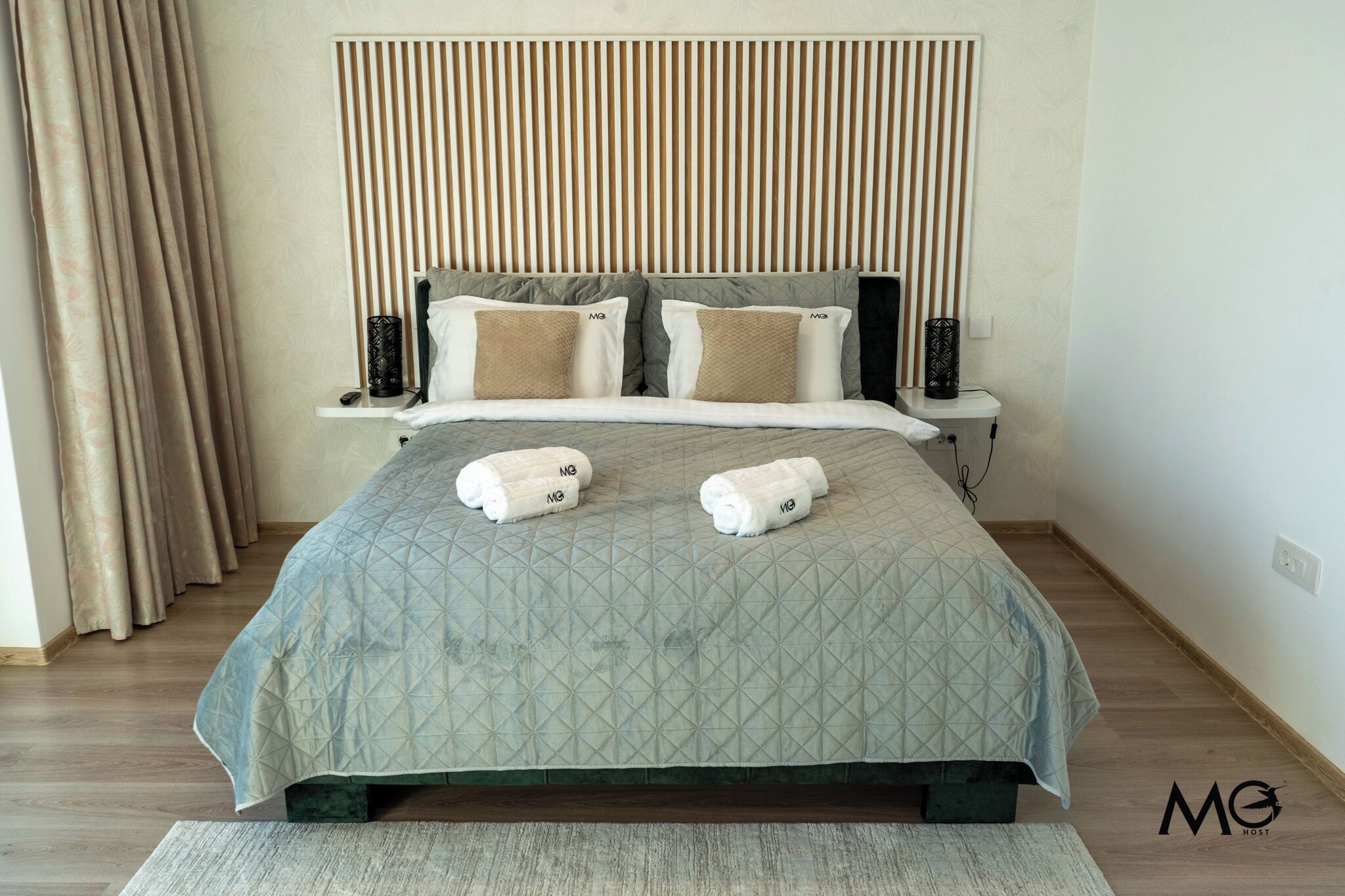 Una cama bien hecha con una colcha acolchada, dos almohadas y dos toallas enrolladas sobre la cama.