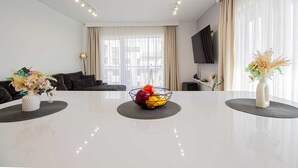 Een moderne woonkamer met een witte tafel, een bank en een aan de muur bevestigde televisie.