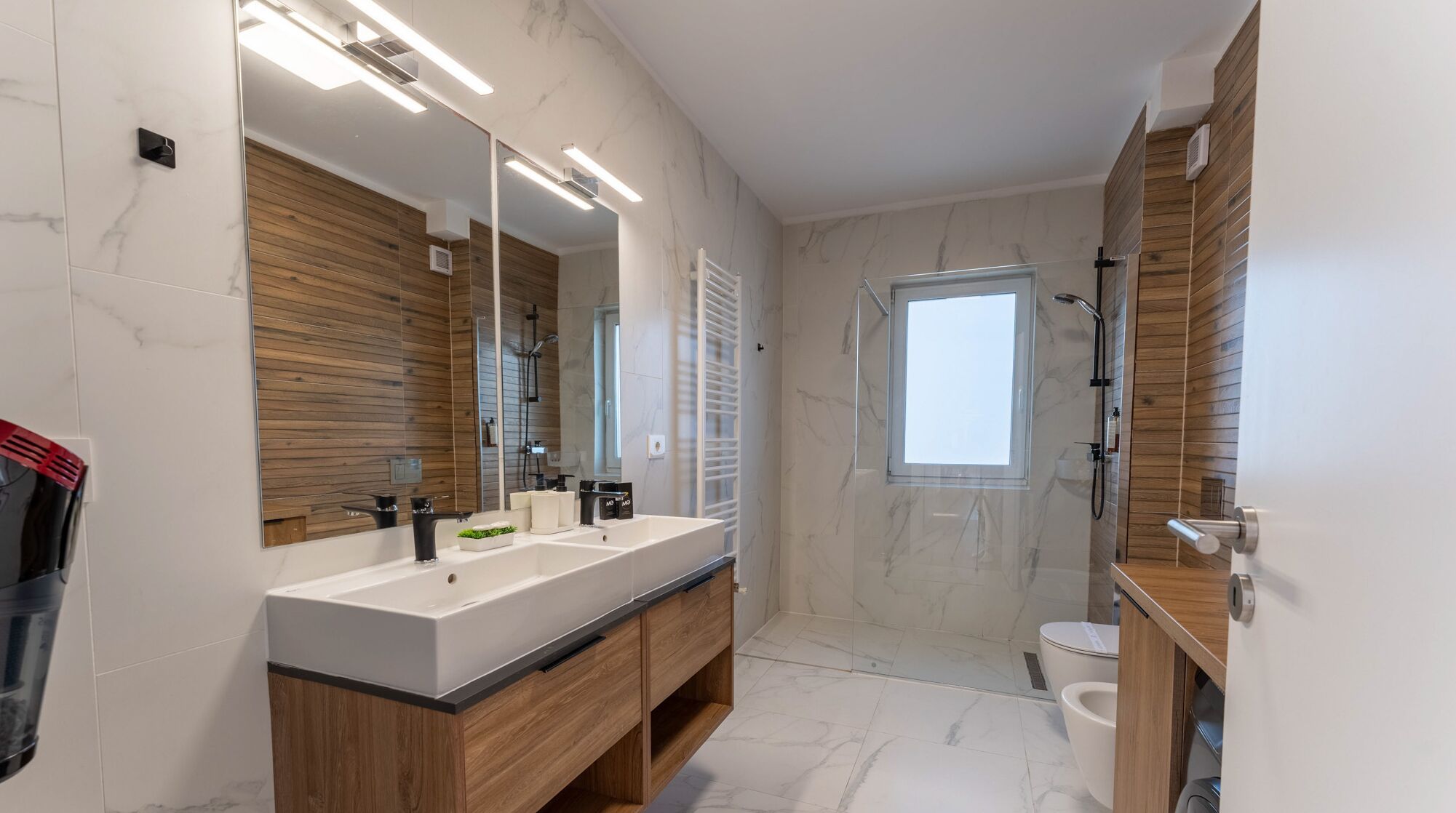 A modern bathroom with a large mirror, two sinks, a shower, and a toilet.