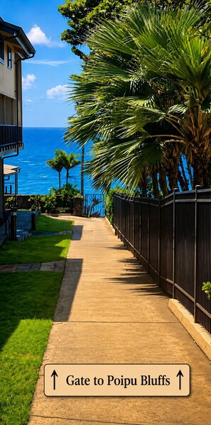 A pathway leading to a gate labeled 'Gate to Poipu Bluffs' with a view of the ocean and palm trees.