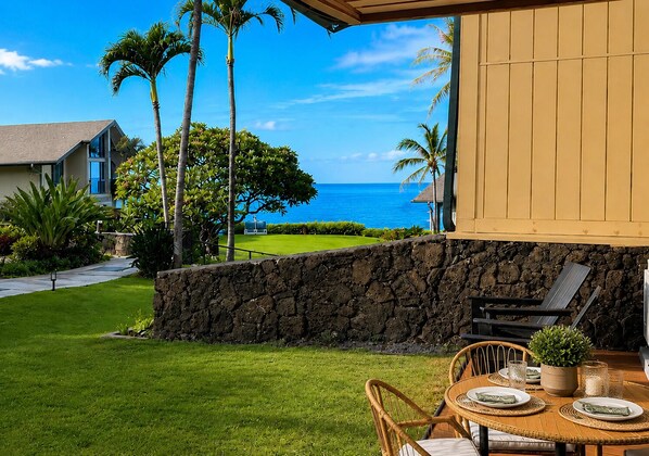 A patio with a stone wall, a dining table set for two, and a view of the ocean.