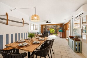 A dining area with a wooden table set for four, black chairs, a hanging light fixture, and a view into the adjacent living space.