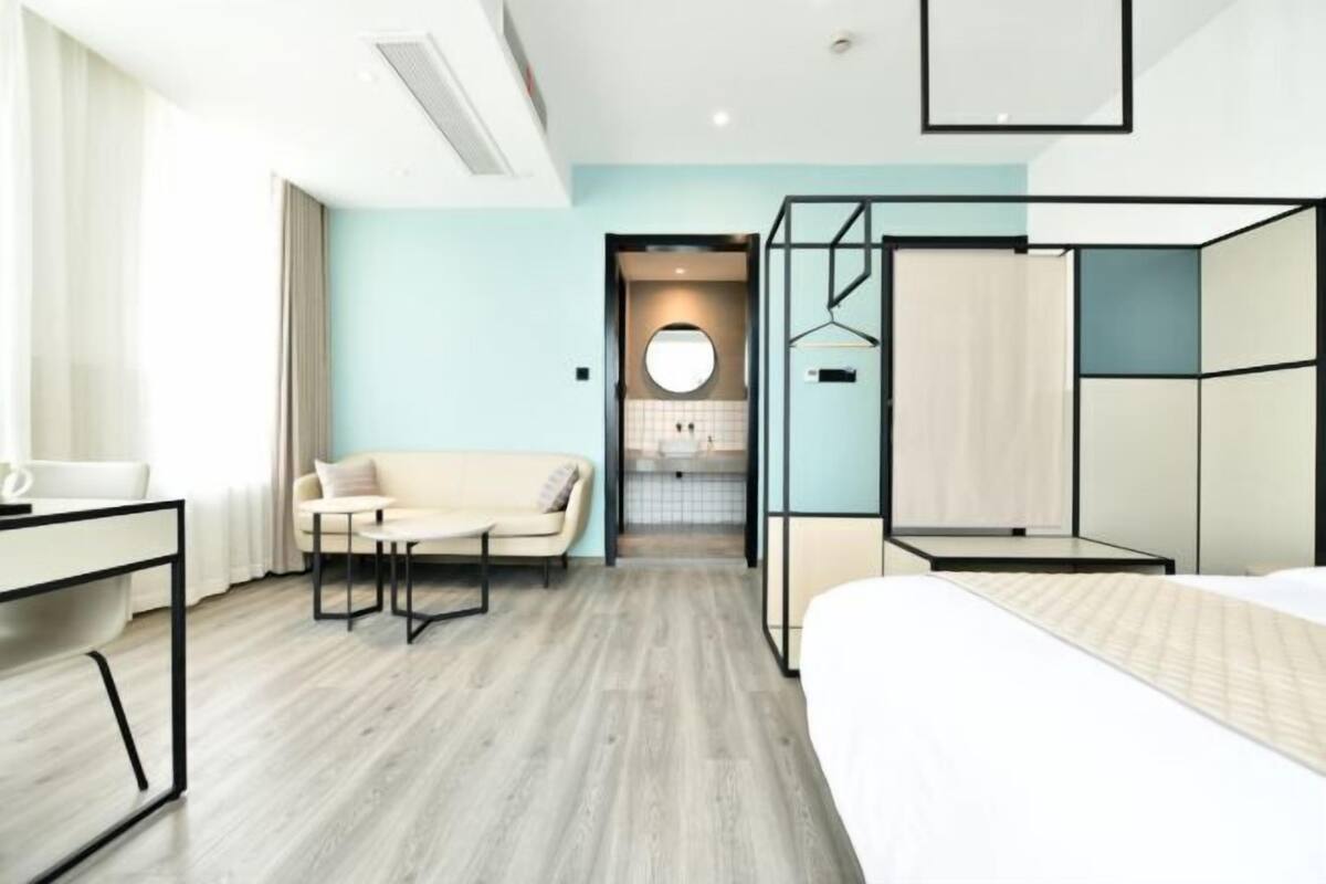 Habitación de hotel moderna con cama, sofá, escritorio y vista al baño.