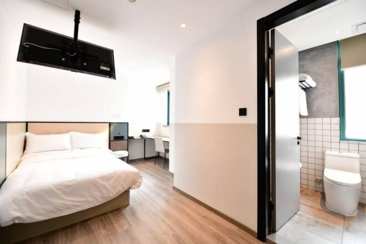 Habitación de hotel moderna con cama, escritorio, silla, inodoro y zona de ducha.