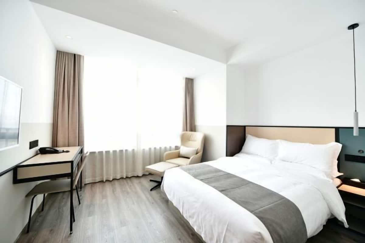 Una habitación de hotel moderna con cama, escritorio, silla y un gran ventanal con cortinas.