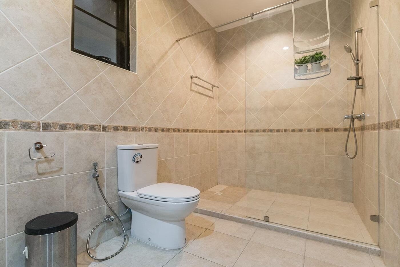 Une salle de bain moderne équipée de toilettes, d’une douche et d’une petite fenêtre située au-dessus des toilettes.