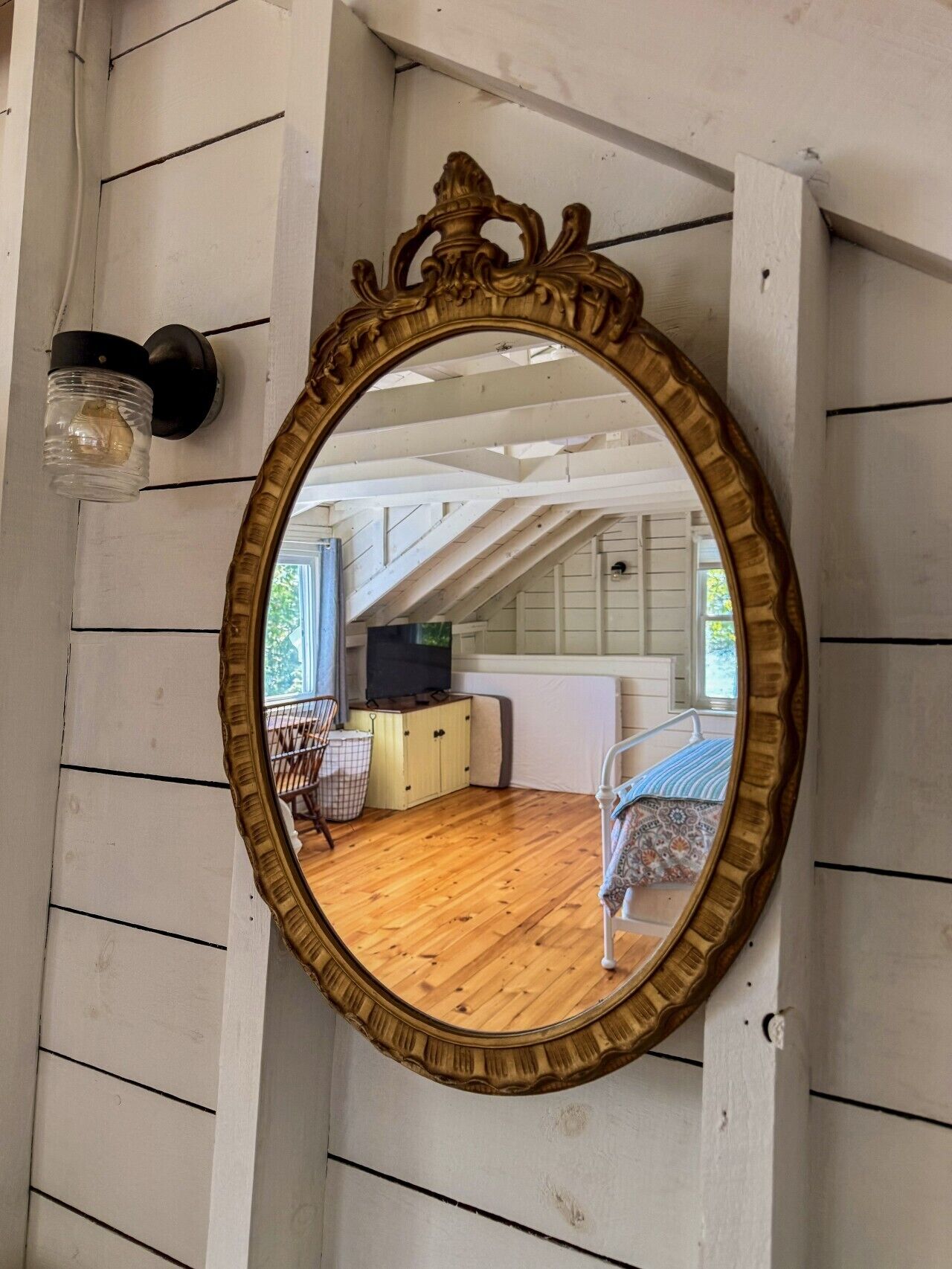 A mirror with an ornate frame, a wooden floor, a television, and a chair.