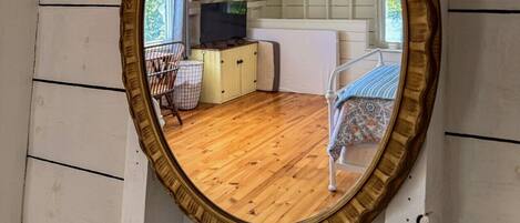 A mirror with an ornate frame, a wooden floor, a television, and a chair.