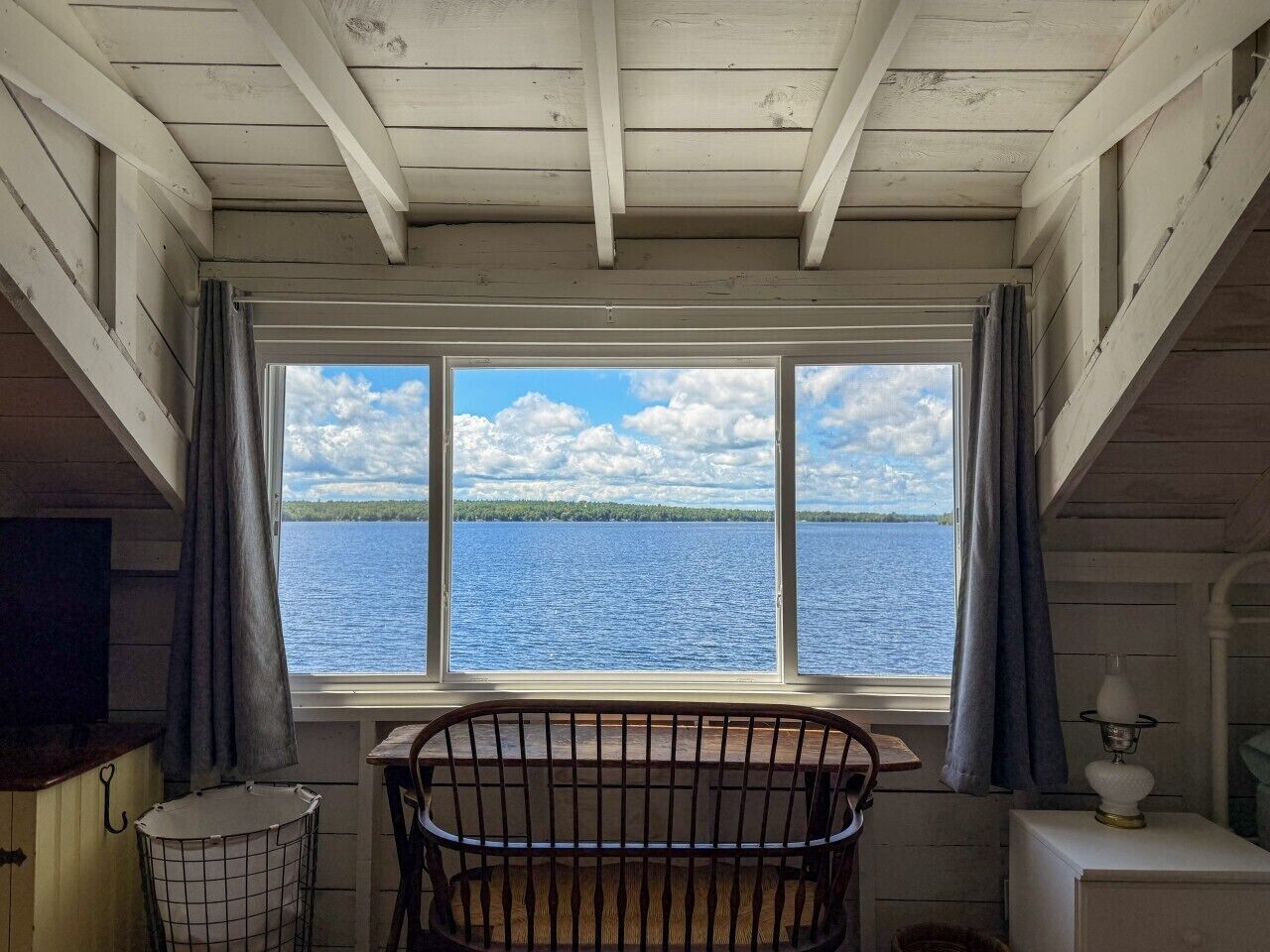 A room with a crib, a window with a view of a lake, and a lamp on a bedside table.
