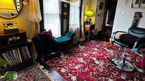 Un salón con alfombra roja, un sofá azul, una silla negra, un mueble de madera con discos, un espejo y una araña.