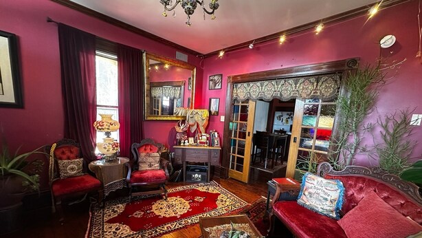 Una habitación con una pared roja, un candelabro, un sofá rojo, una mesa de centro de madera y una alfombra estampada.