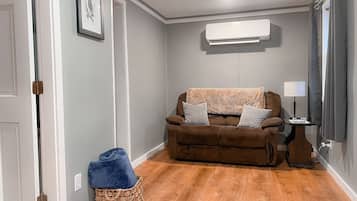 Ein Wohnzimmer mit einem braunen Sofa, einem blauen Kissen, einem Korbwäscher und einer weißen Klimaanlage an der Wand.