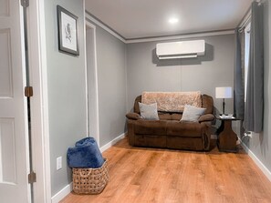 Ein Wohnzimmer mit einem braunen Sofa, einem blauen Kissen, einem Korbwäscher und einer weißen Klimaanlage an der Wand.