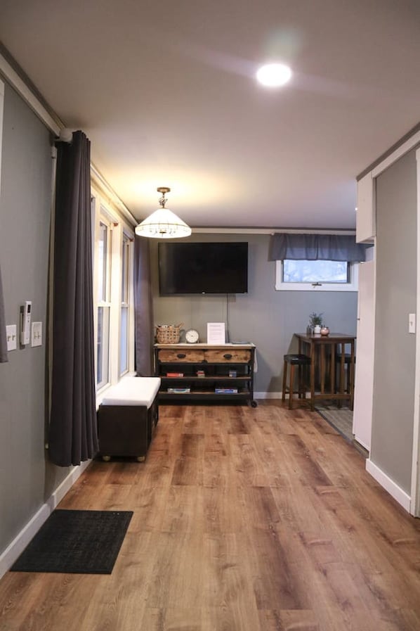 A hallway with wooden flooring, a bench, a television mounted on the wall, and a small table with a chair.