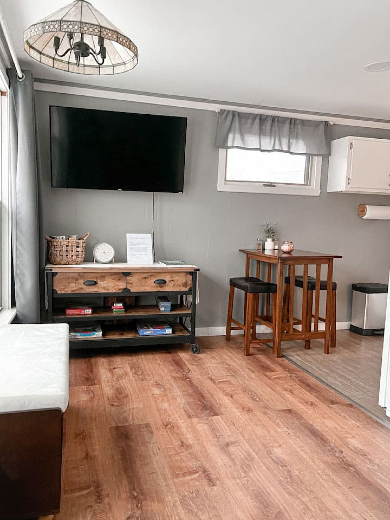 Een woonkamer met een flatscreen televisie, een houten salontafel, een eettafel met stoelen, een rieten mand en een prullenbak.
