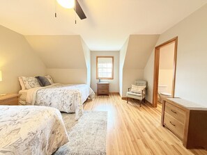 A bedroom with two beds, a chair, a dresser, and a window. - Modern Lakeside Home (Glenburn)