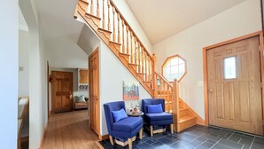 A staircase leading to a second floor, a wooden door, and two blue chairs in a hallway. - Modern Lakeside Home (Glenburn)