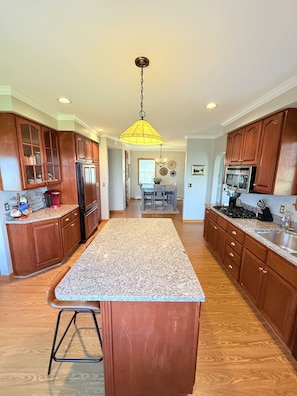 A kitchen with wooden cabinets, granite countertops, a central island, and a hanging pendant light.