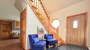 A staircase with wooden balusters, a door with a window, and two blue armchairs with a small table between them. - Modern Lakeside Home (Glenburn)