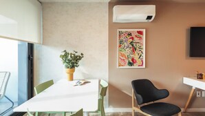 A modern room with a white table, green chairs, a potted plant, an air conditioner, and a colorful abstract painting on the wall. - Casa Rosada (Mar del Plata)