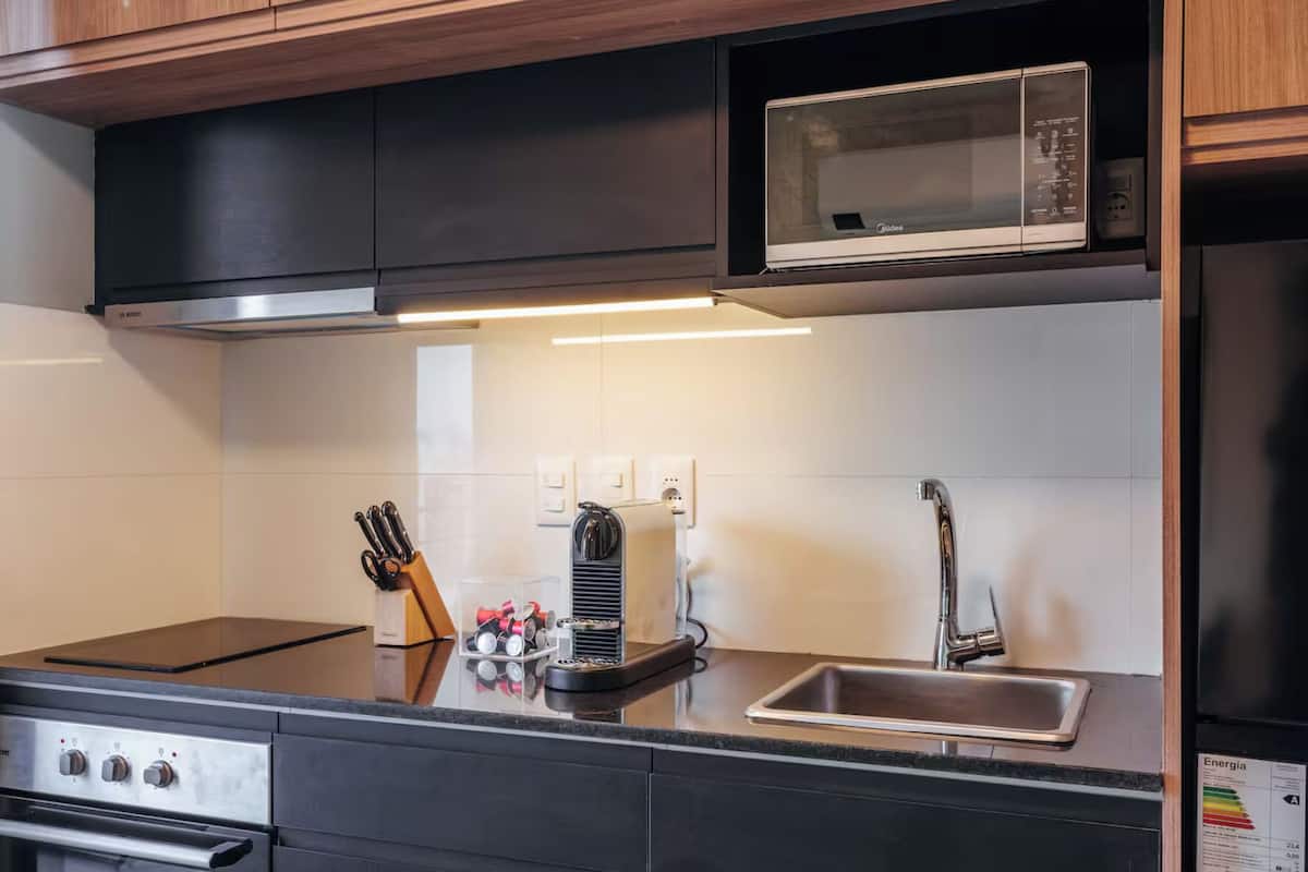 A modern kitchen with a microwave, stove, and sink. There are knives and a container with kitchen utensils.