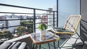 A balcony with a glass table, a wicker chair, and a potted plant. - Casa Rosada (Mar del Plata)