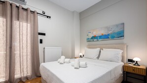 Un lit bien fait, avec du linge de lit et des serviettes blanches, une table de chevet avec une lampe, un tableau au mur et une fenêtre avec des rideaux.