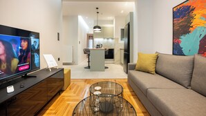 Un salon moderne avec un téléviseur à écran plat, un canapé, une table basse et une cuisine en arrière-plan.