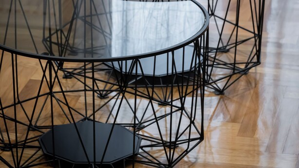 Une pièce moderne dotée de trois tables à plateaux en verre et à structure métallique, d’un parquet en bois et d’une fenêtre ornée de rideaux légers.