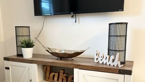 Una sala de estar moderna con un televisor de pantalla plana montado en la pared, una consola de madera con un cuenco decorativo, y un letrero que dice "Beach".