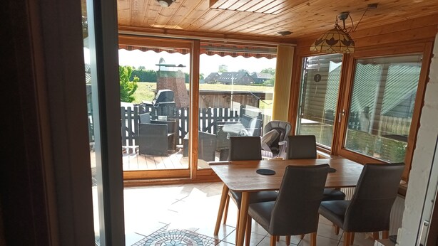 Un comedor con mesa y sillas de madera, vista del patio exterior con una parrilla, y un ventanal con vistas del entorno.