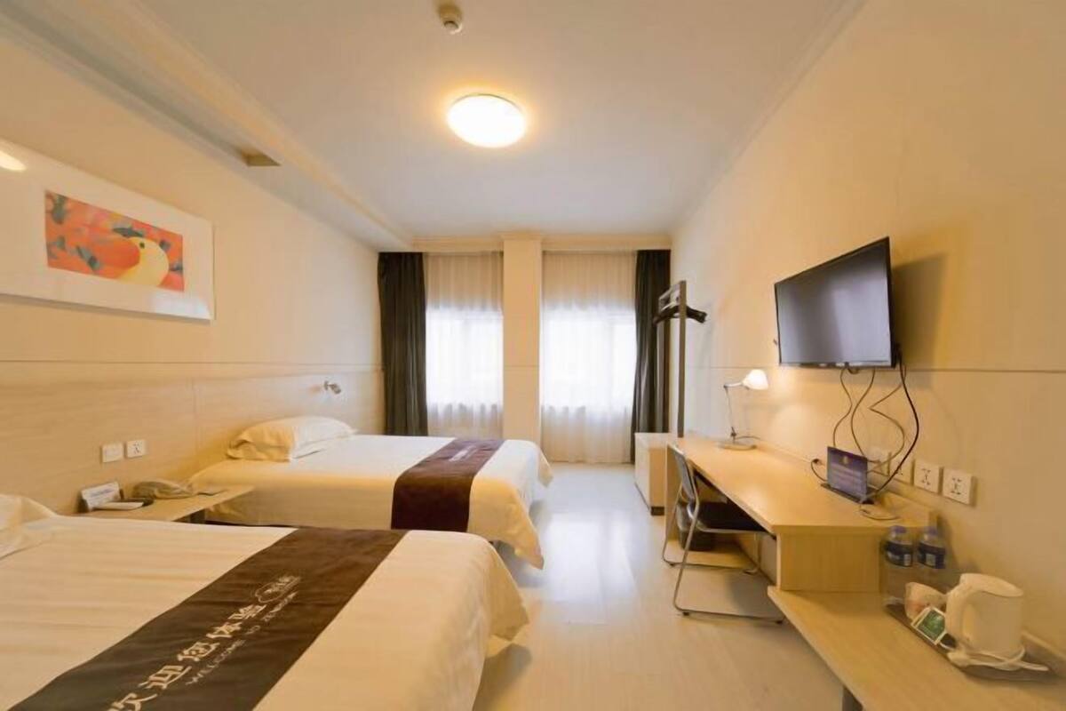 A hotel room with two beds, a desk, a television, and a window with curtains.