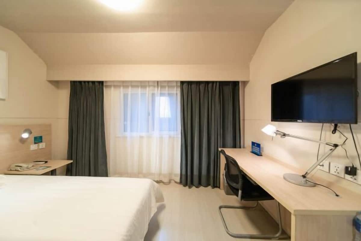 A hotel room with a bed, desk, chair, TV, and curtains.