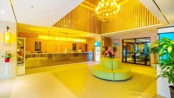 A modern lobby with a reception desk, a central seating area, and a staircase leading to upper floors.