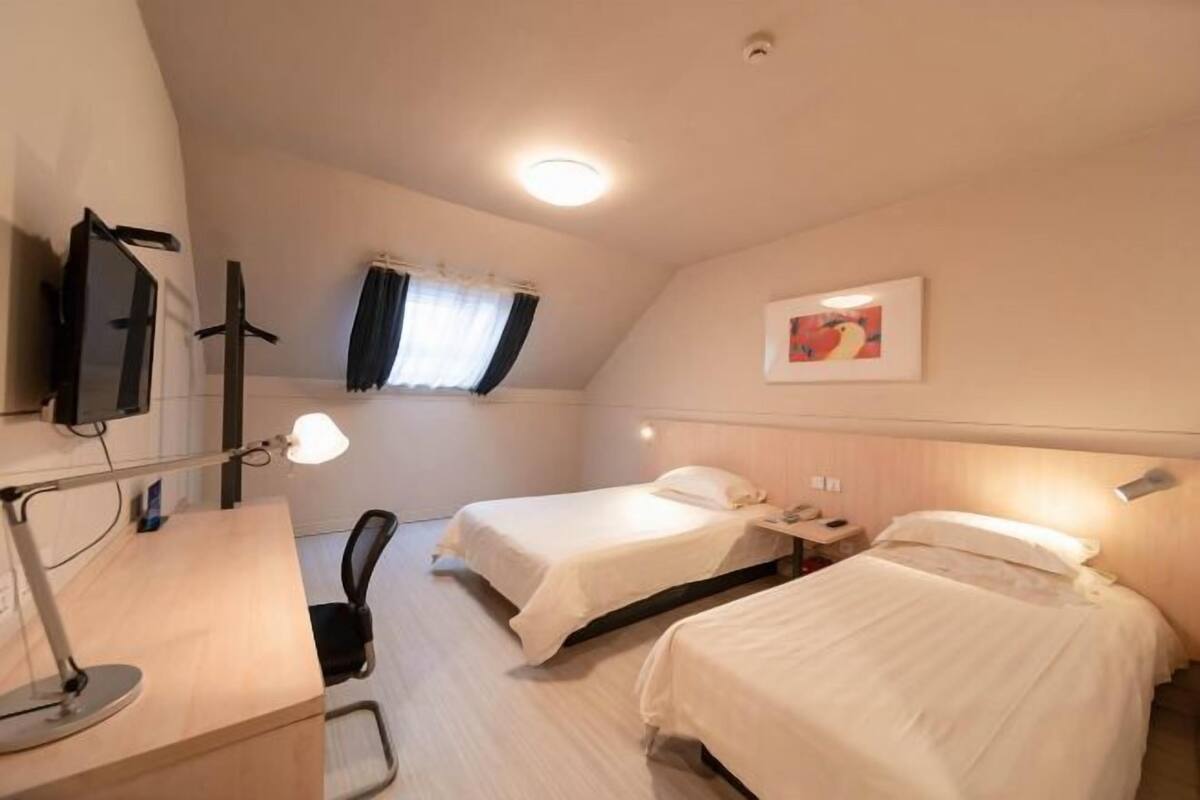 A hotel room with two beds, a desk with a lamp, a TV, and a window with curtains.