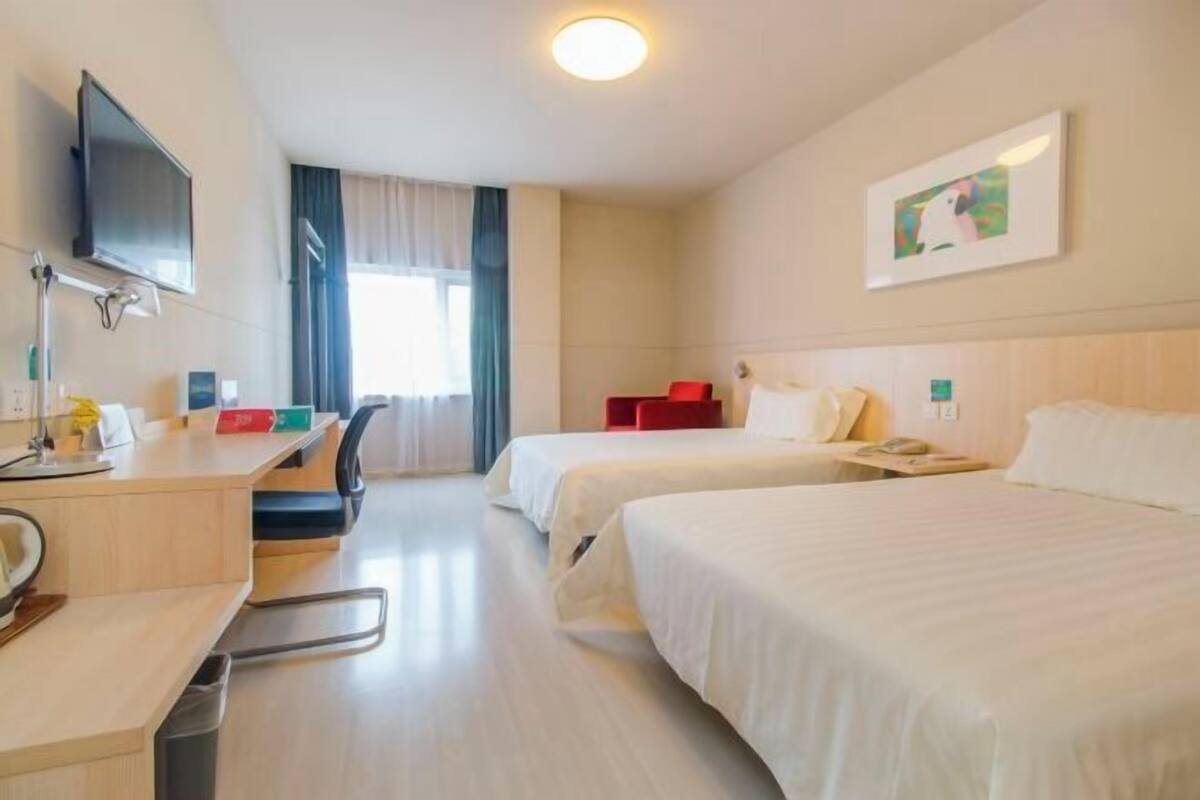 A hotel room with two beds, a desk with a chair, a TV, and a window with curtains.