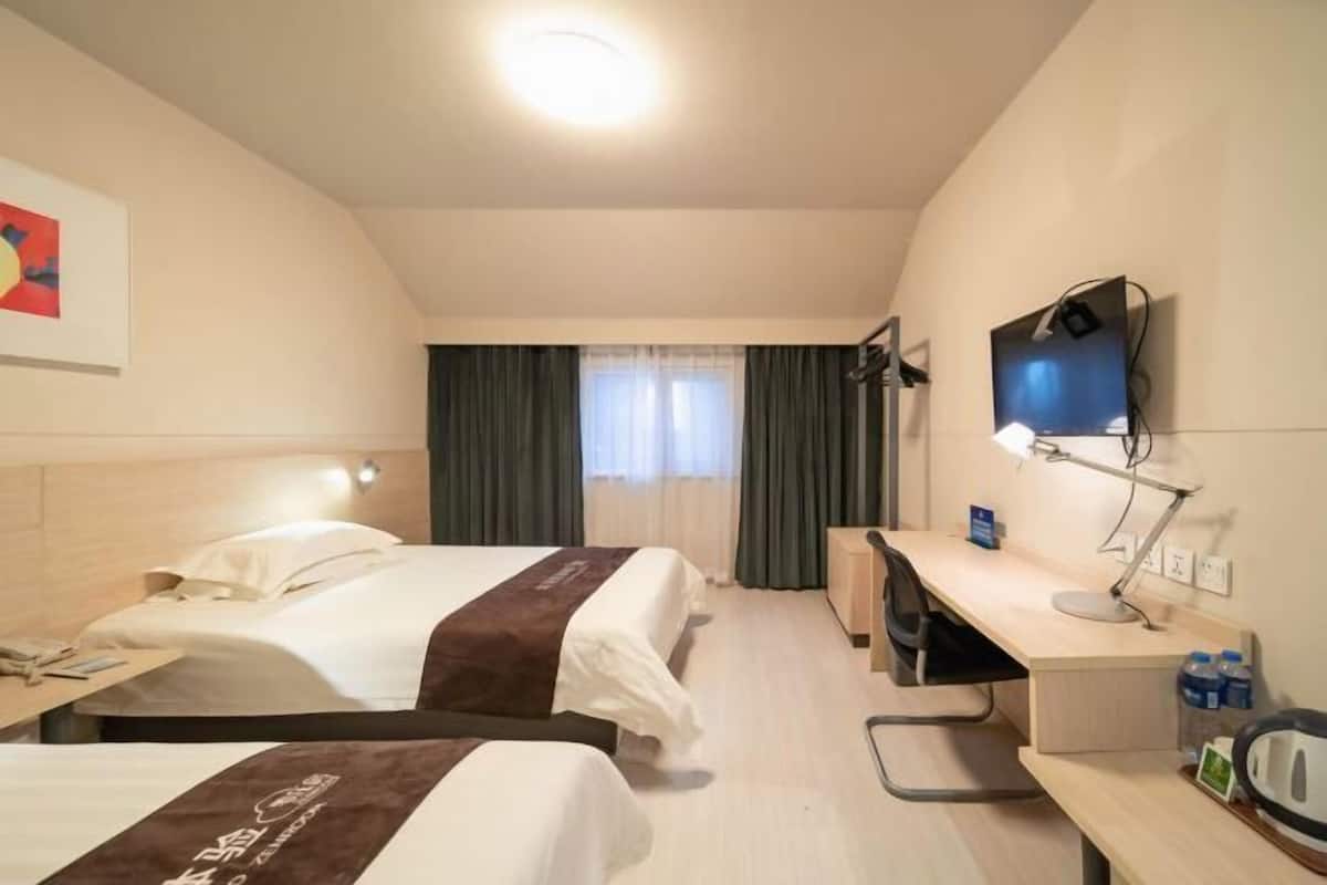 A hotel room with two beds, a desk, a chair, a television, and a window with curtains.