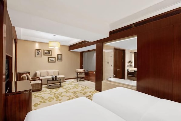 A hotel room with a bed, a sofa, a small table, a TV, and a bathroom visible through an open door.